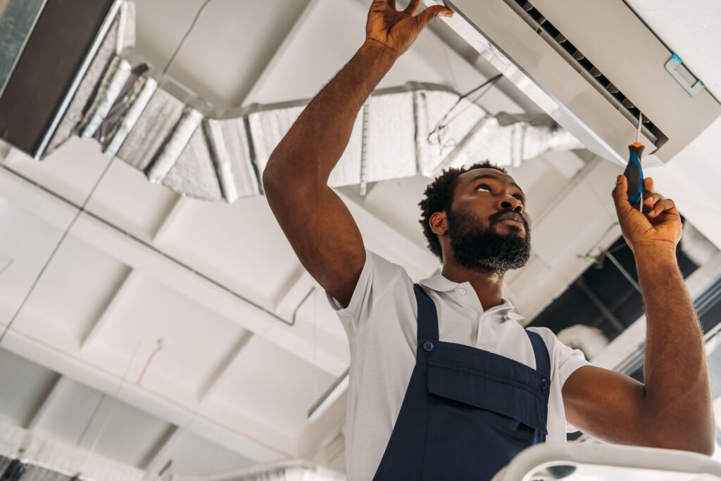 low angle view of african american handyman repairing air conditioner with screwdriver